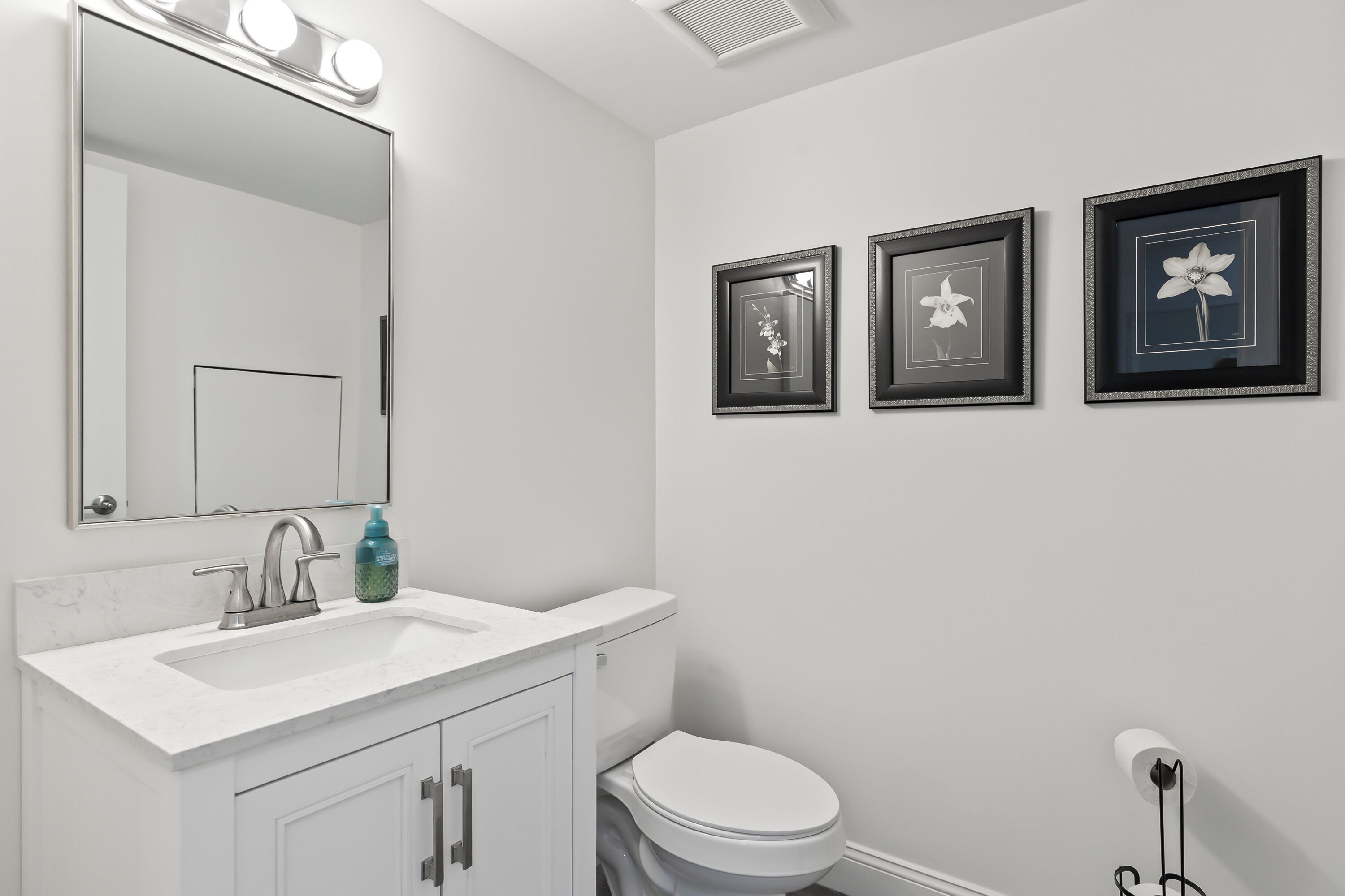A bathroom with a white sink, mirror, and toilet. There are three framed pictures on the wall.