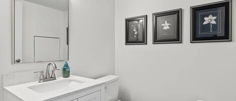 A bathroom with a white sink, mirror, and toilet. There are three framed pictures on the wall.