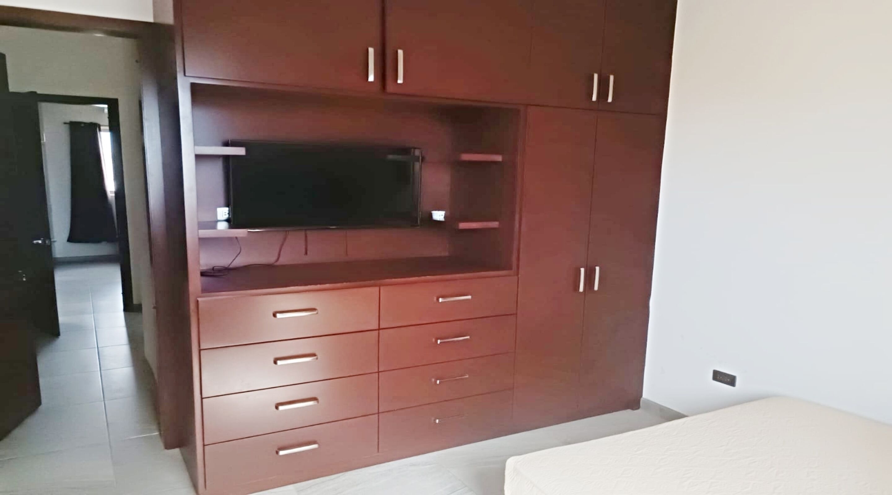 Una stanza con mobile TV a incasso, un letto e una porta che dà accesso a un'altra stanza.