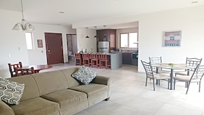 Ein modernes Wohnzimmer mit einer Couch, einem Esstisch mit Stühlen, einer Küchenzeile mit Bar und einem großen Fenster.