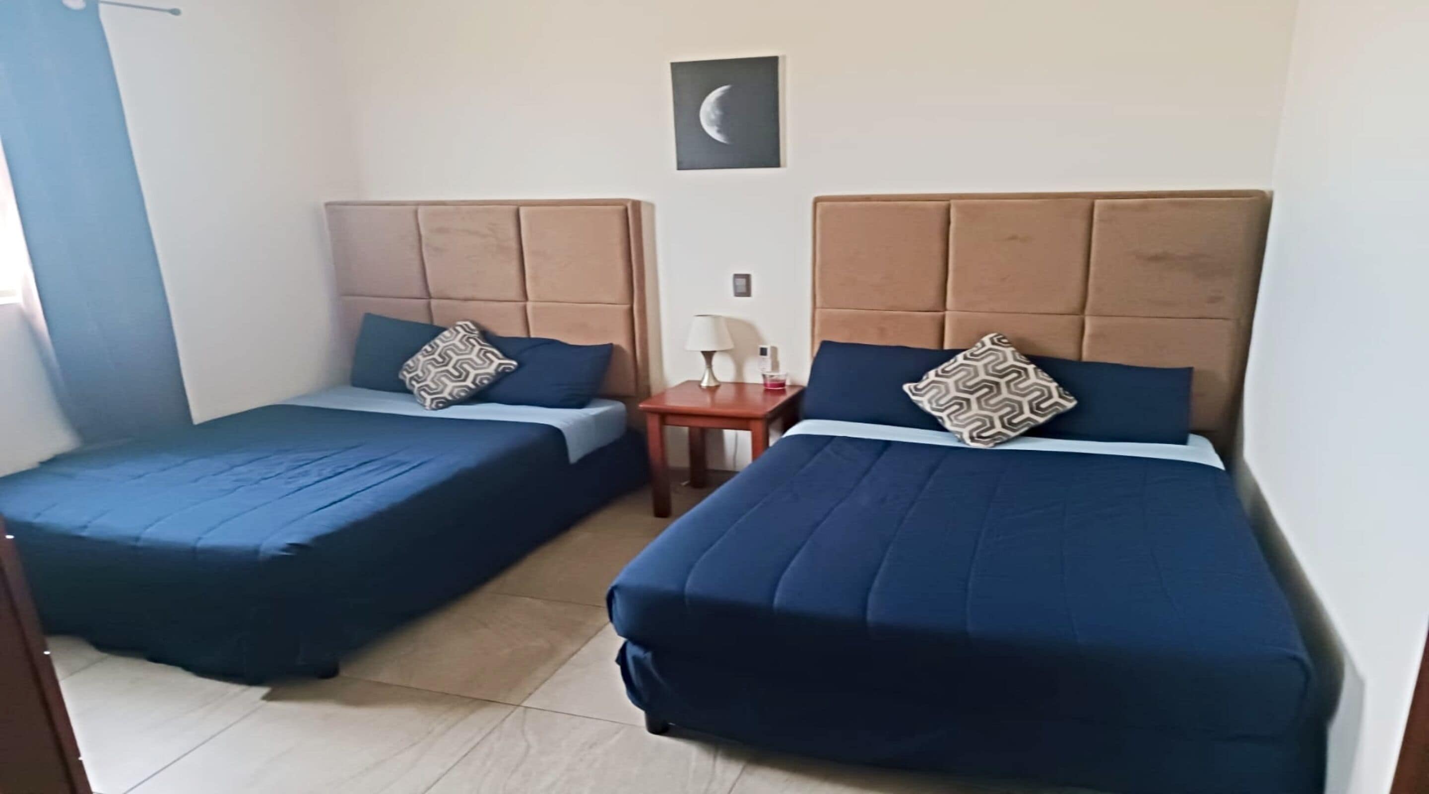 A hotel room with two beds, each with a headboard, a nightstand, and a wall-mounted lamp.