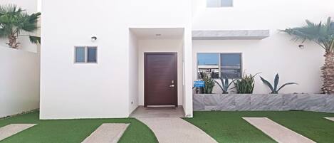 A modern two-story house with a central entrance, a small porch, and a well-maintained lawn.