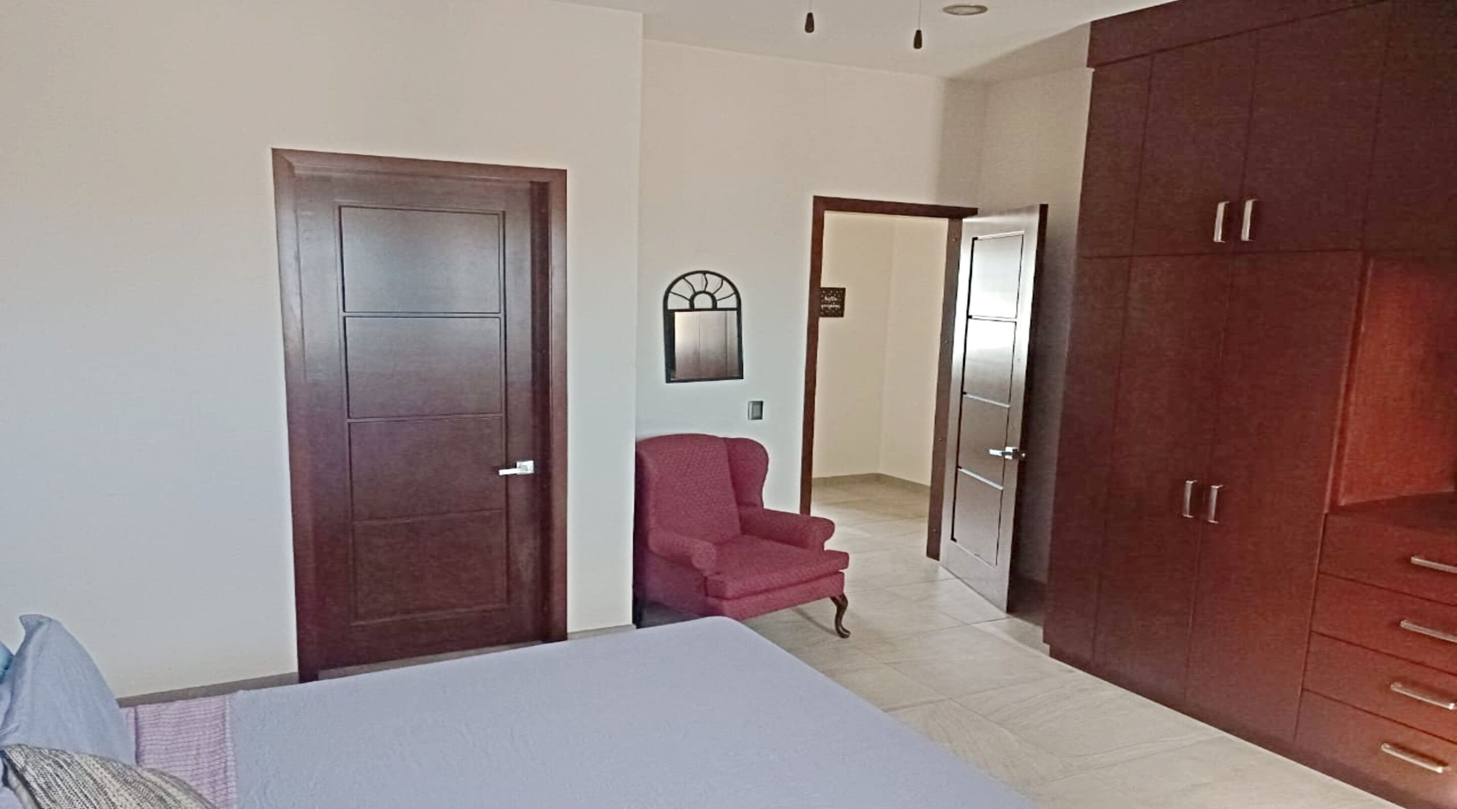 A bedroom with a bed, a red armchair, a wardrobe, and a door.