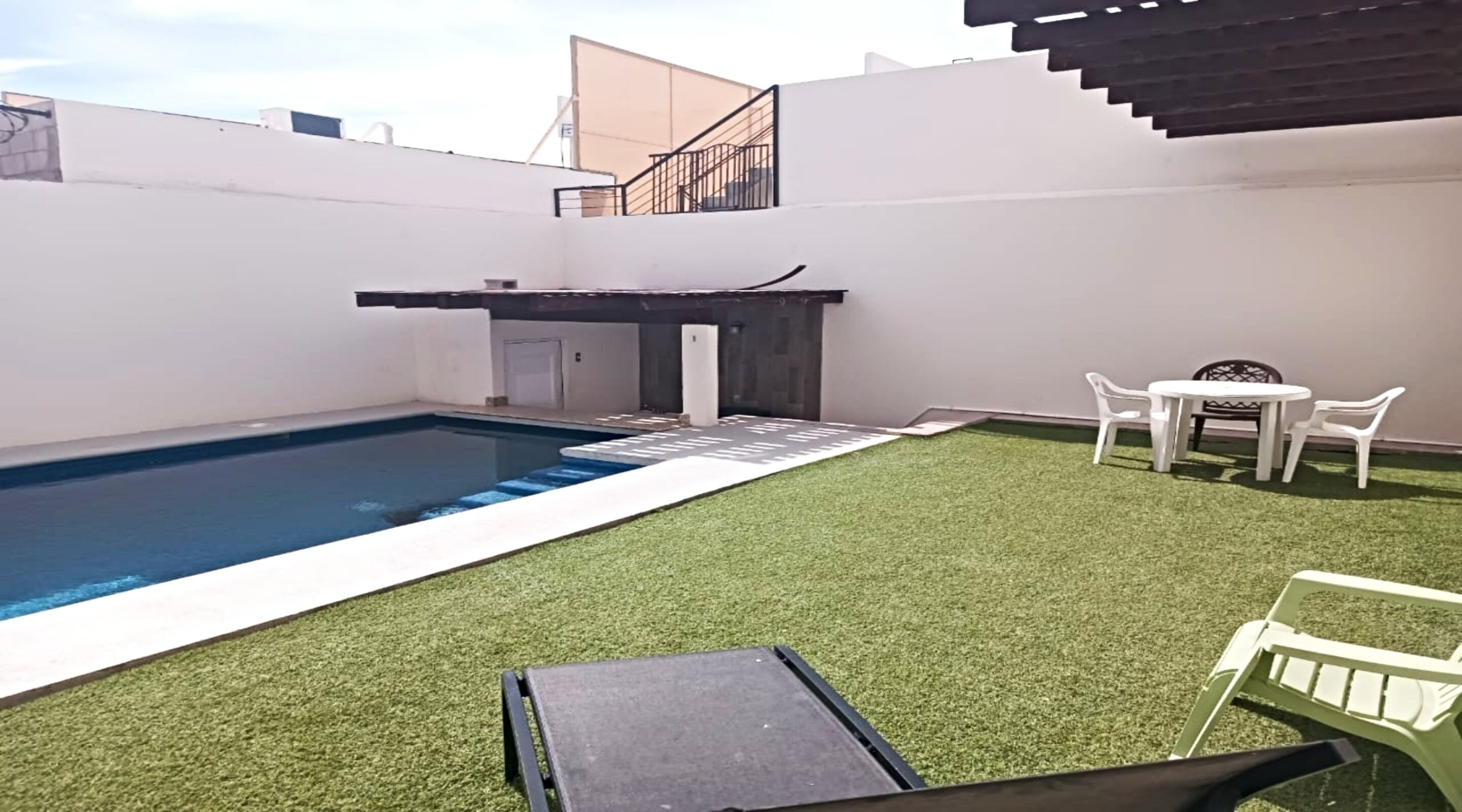 A rooftop pool with artificial grass, a small table, and two chairs.