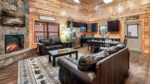 A cozy cabin interior with a stone fireplace, leather furniture, a kitchen area, and a dining space. - Pet Friendly! Private Pool, Mini Golf, Views! (Pigeon Forge)