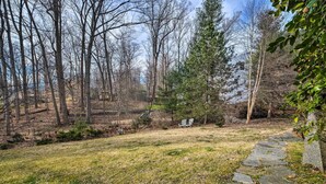 A stone pathway leading to a grassy area with two white chairs, surrounded by trees and a house in the background. - 3 Mi to NIH! Spacious Bethesda Apt w/ Yard (Bethesda)