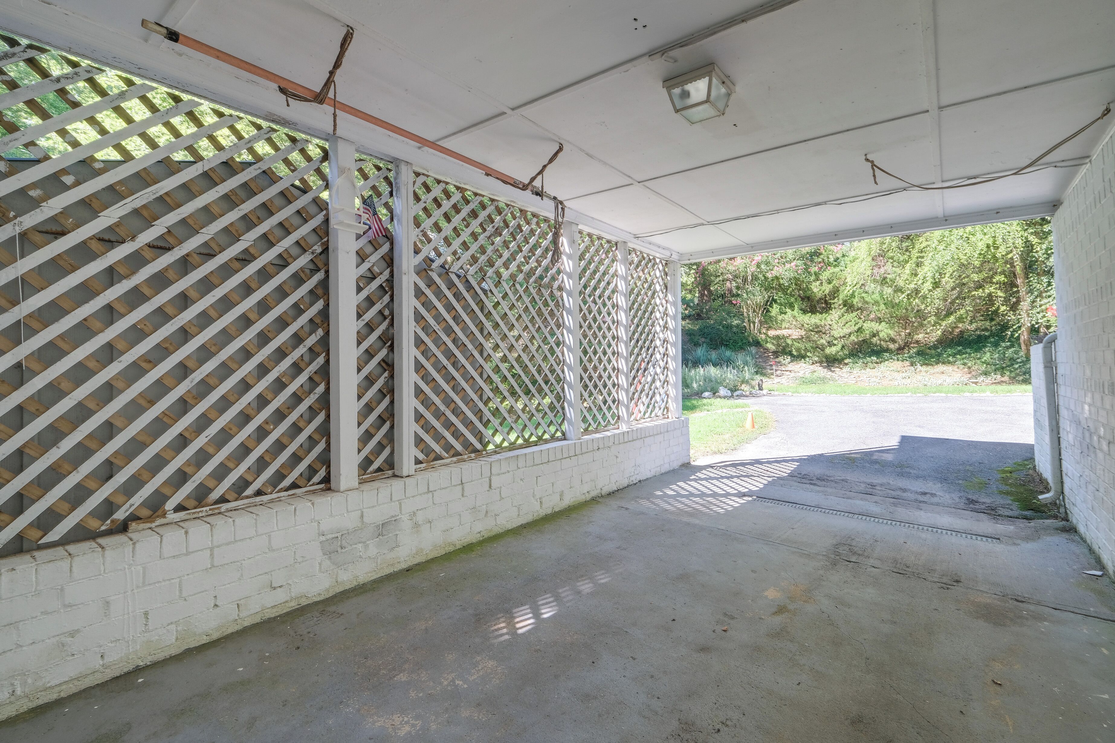 Un espace extérieur abrité doté d’un sol en béton, de murs en briques blanches et de panneaux en treillis.