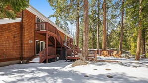 Una baita di legno con un balcone, immersa tra alberi alti e neve a terra.