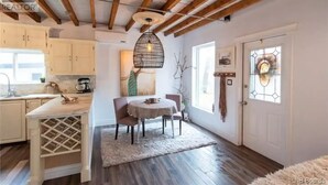 A cozy kitchen with wooden beams, a dining area with a round table, and a large window with a stained glass door. - Private house/large hottub/sauna & optional "Adult/Red room" (Rothesay)