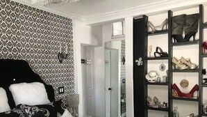 A bedroom with a patterned wallpaper, a black and white bed, a mirror, and a shoe rack with various footwear. - Private house/large hottub/sauna & optional "Adult/Red room" (Rothesay)