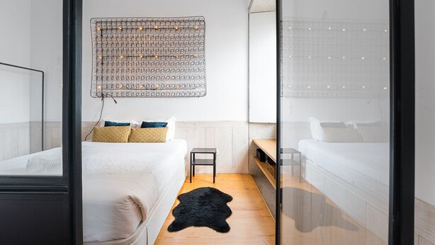 Et moderne hotelværelse med to senge, en sort, lodden måtte og et dekorativt vægophæng.