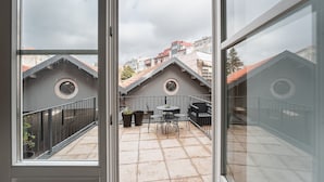 En balkon med flisegulv, to plantekasser og et bord med stole.