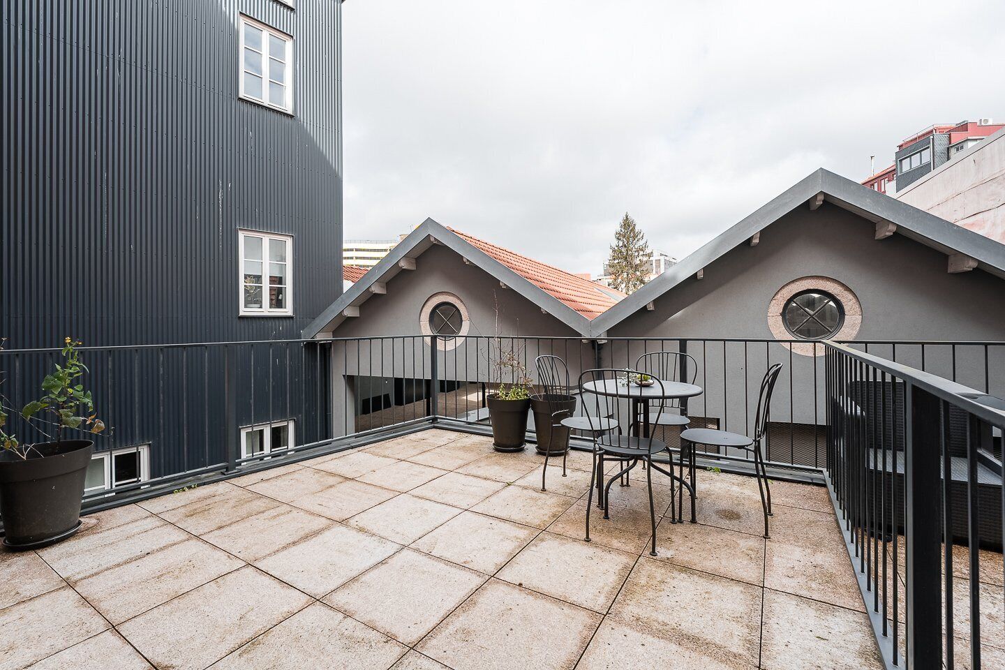 Eine Dachterrasse mit gefliestem Boden, einem runden Tisch mit Stühlen und Topfpflanzen.