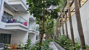 A narrow pathway flanked by lush greenery and tall palm trees, leading to a building with balconies and a ceiling fan. - Rasa Sayang at The Loft Imago (Kota Kinabalu)