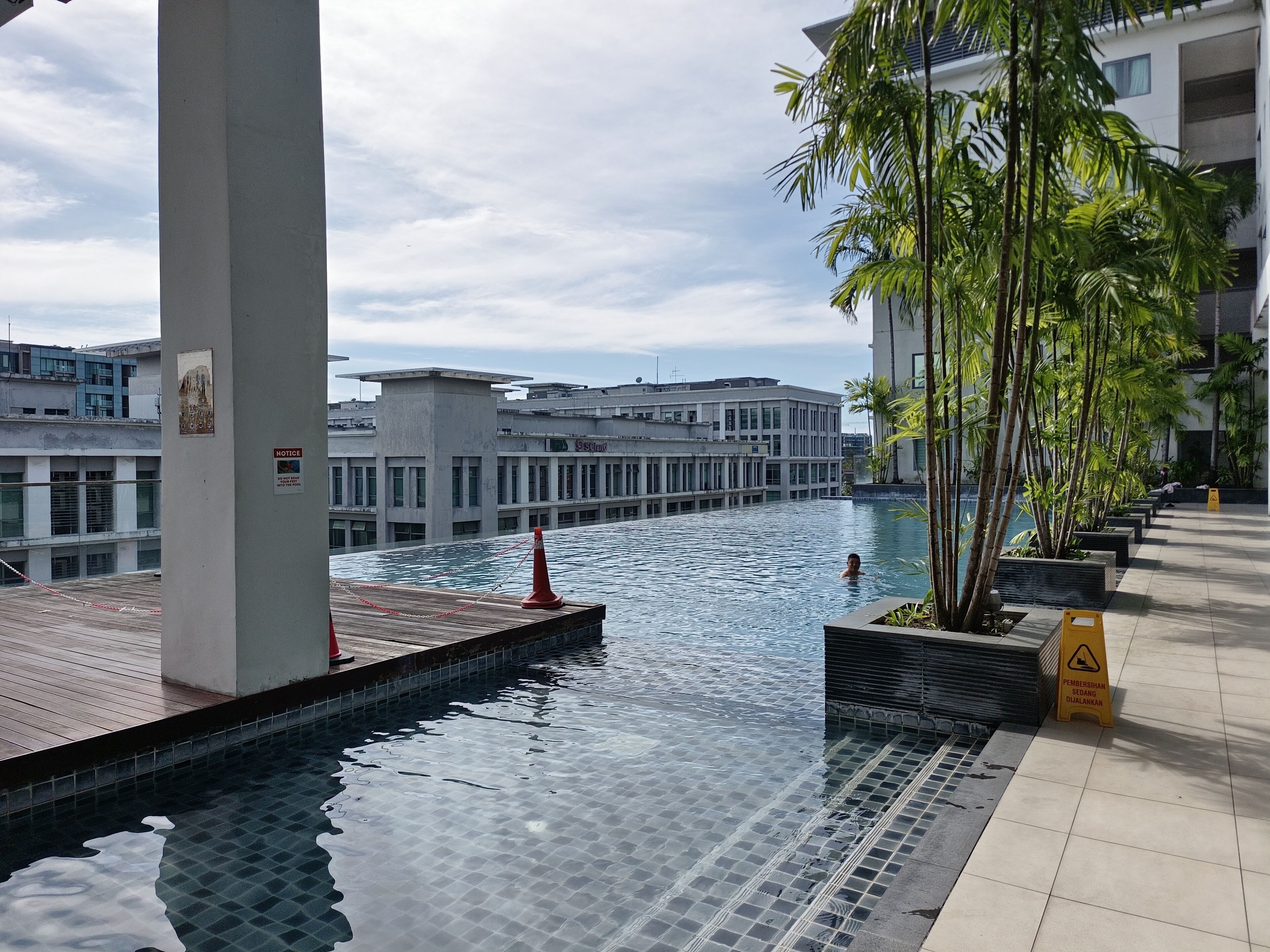 A swimming pool with a tiled deck, surrounded by buildings and palm trees.