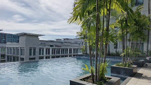 A swimming pool with a modern design, surrounded by tall palm trees and a building with a glass facade in the background. - Rasa Sayang at The Loft Imago (Kota Kinabalu)