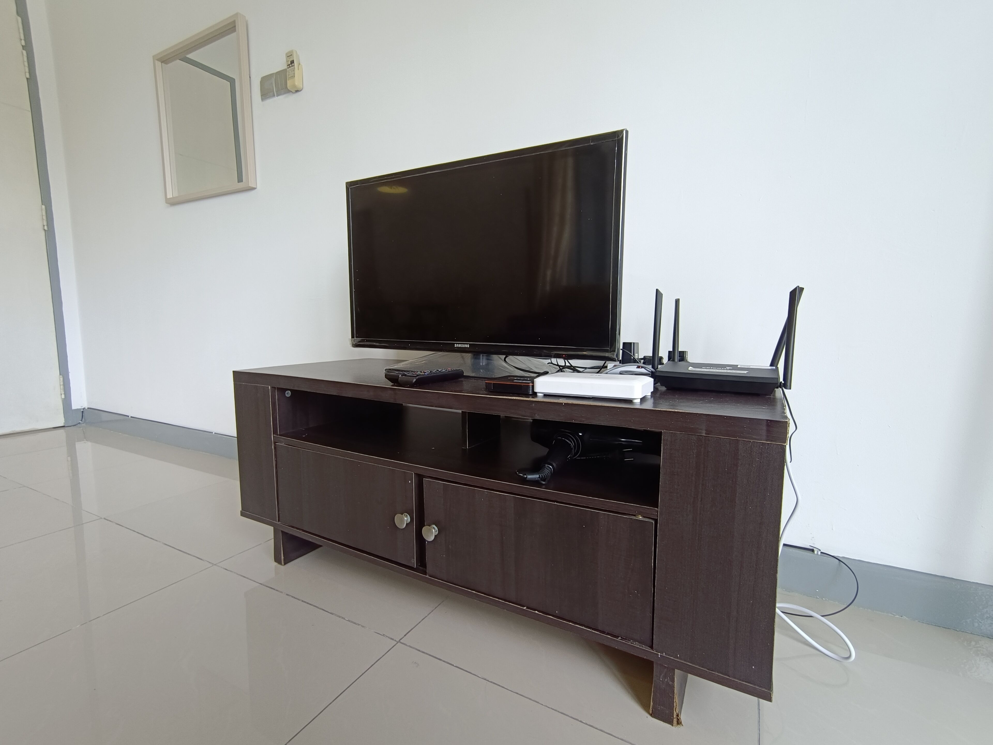 Un mueble de madera oscura con un televisor de pantalla plana, un control remoto y un dispositivo electrónico blanco.