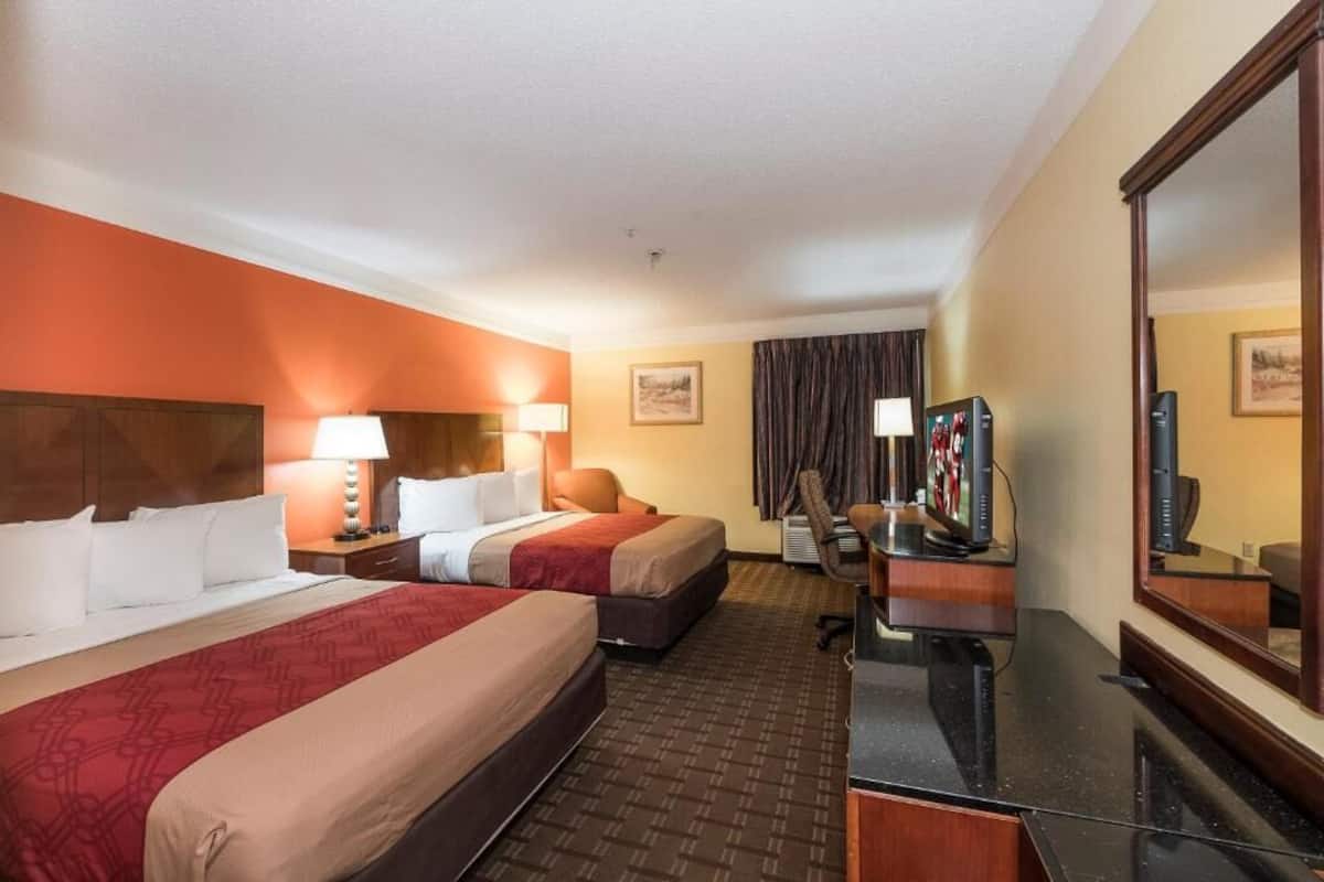 A hotel room with two beds, a desk with a computer, a TV, and a large mirror.