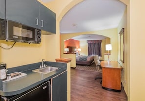 Habitación de hotel compacta con kitchenette, una cama, un escritorio y una pequeña zona de estar.