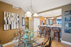 Un coin repas avec une table en verre, des chaises en osier et une cuisine en arrière-plan.