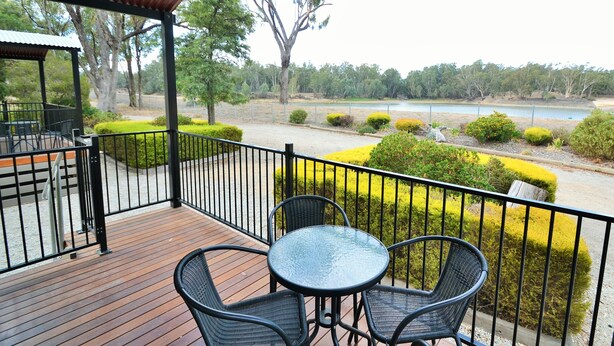 A covered outdoor area with a wooden deck, black metal chairs, and a glass table. - Torrumbarry Weir Holiday Park (Patho)