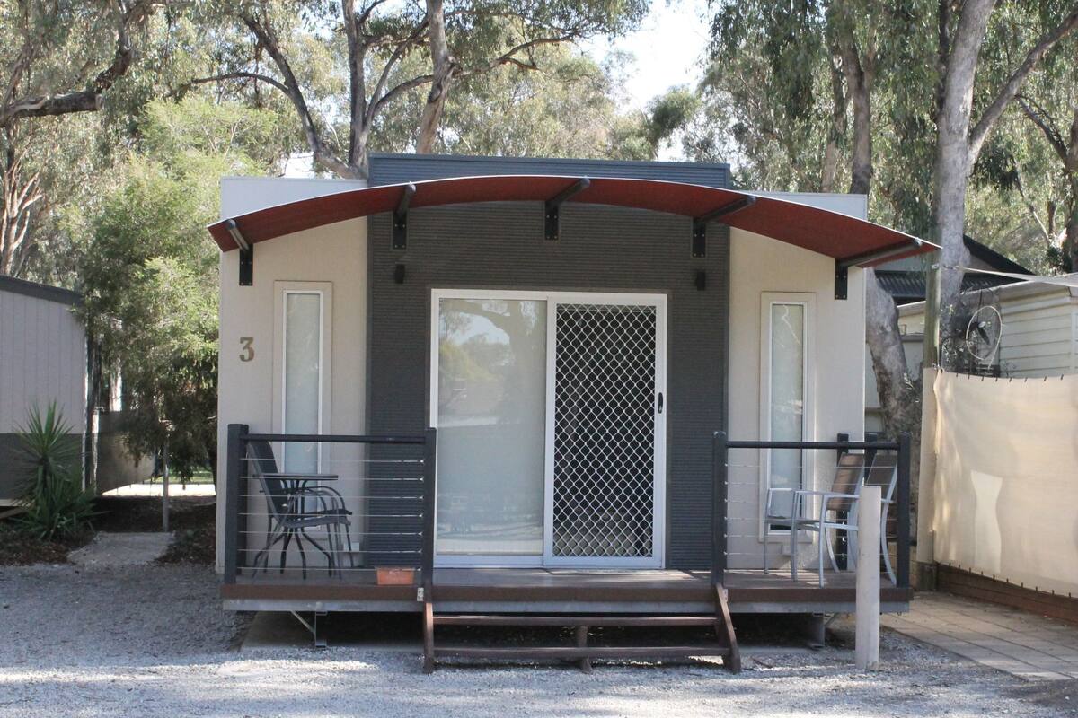 A small, single-story mobile home with a covered porch, numbered 3, featuring a sliding glass door and a metal security gate.