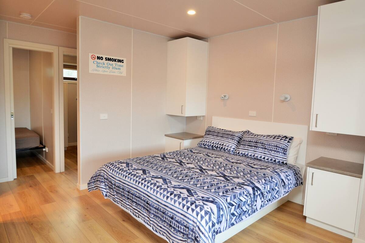 A bedroom with a bed, a wardrobe, a 'NO SMOKING' sign, and a door leading to another room.