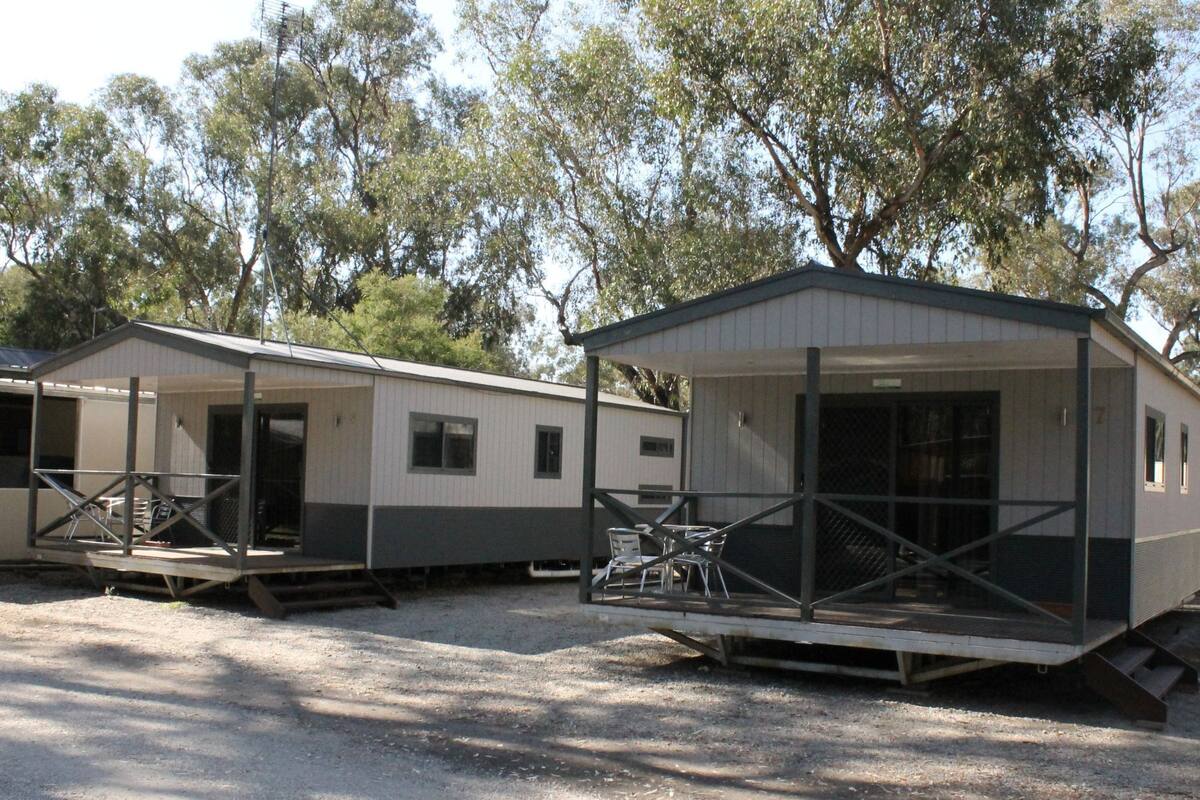 A mobile home with a porch and a small deck, surrounded by trees.