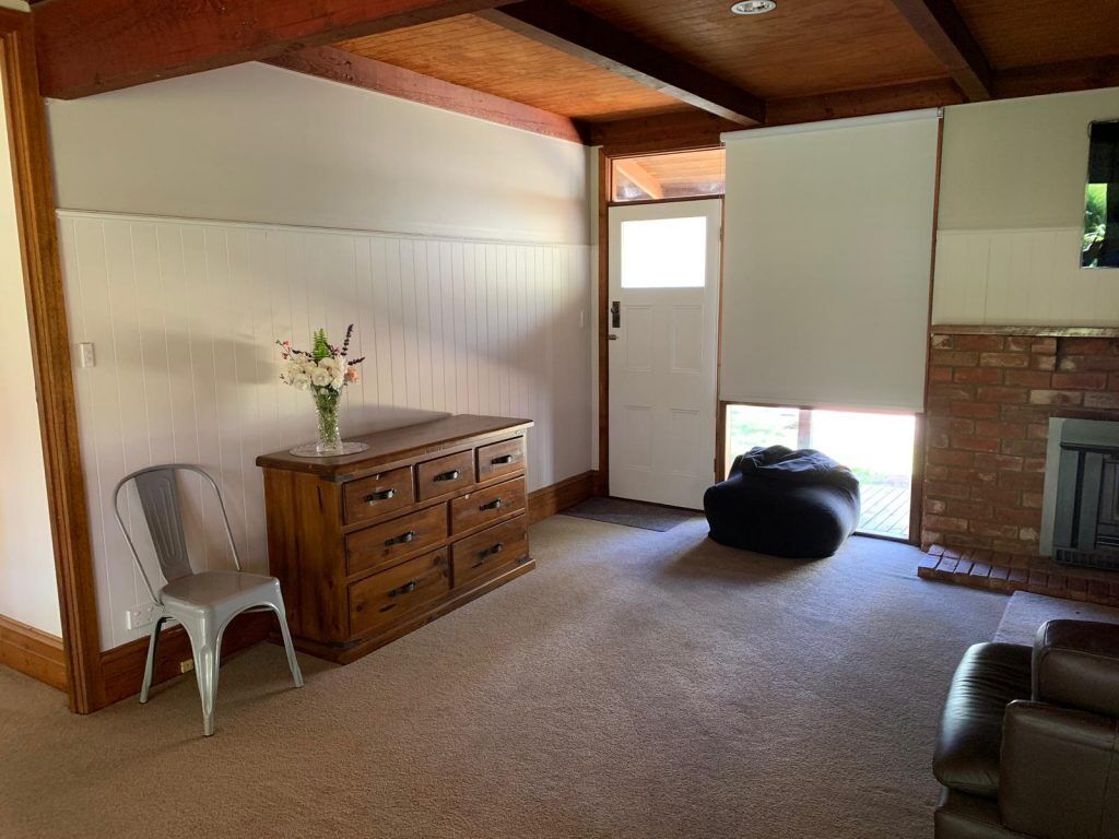 A spacious living room with a wooden dresser, a white chair, a black bean bag, and a fireplace.