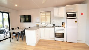 A modern kitchen with white cabinets, a dining table with chairs, a flat-screen TV mounted on the wall, and a microwave above the stove. - Torrumbarry Weir Holiday Park (Patho)