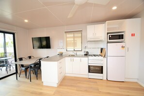 Una cocina moderna con armarios blancos, una mesa de comedor con sillas, un televisor de pantalla plana montado en la pared y un microondas sobre la estufa.