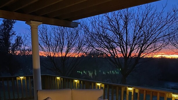 A deck with a fire feature, seating, and a view of the sunset.