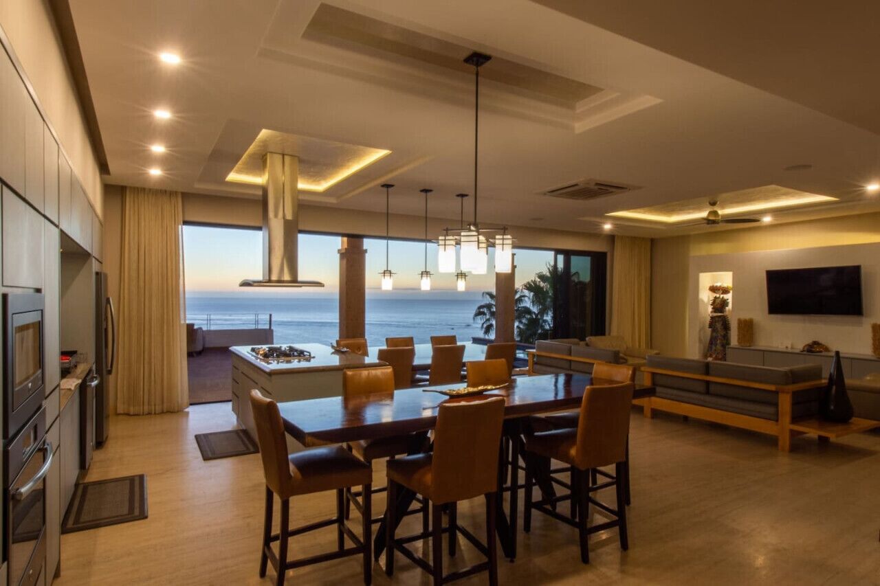 A modern kitchen with a large island, dining area with chairs, and a view of the ocean.
