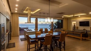 Une cuisine moderne dotée d’un grand îlot central, d’un coin repas avec des chaises et d’une vue sur l’océan.