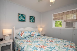 A bedroom with a bed, two bedside tables with lamps, a ceiling fan, and two framed pictures on the wall. - Park and Walk! Downtown Rehoboth Beach Condo (Rehoboth Beach)