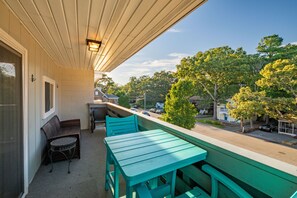 A balcony with a table and chairs, overlooking a street with houses and trees.