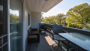 A balcony with a glass door, a table, and two chairs. - Park and Walk! Downtown Rehoboth Beach Condo (Rehoboth Beach)