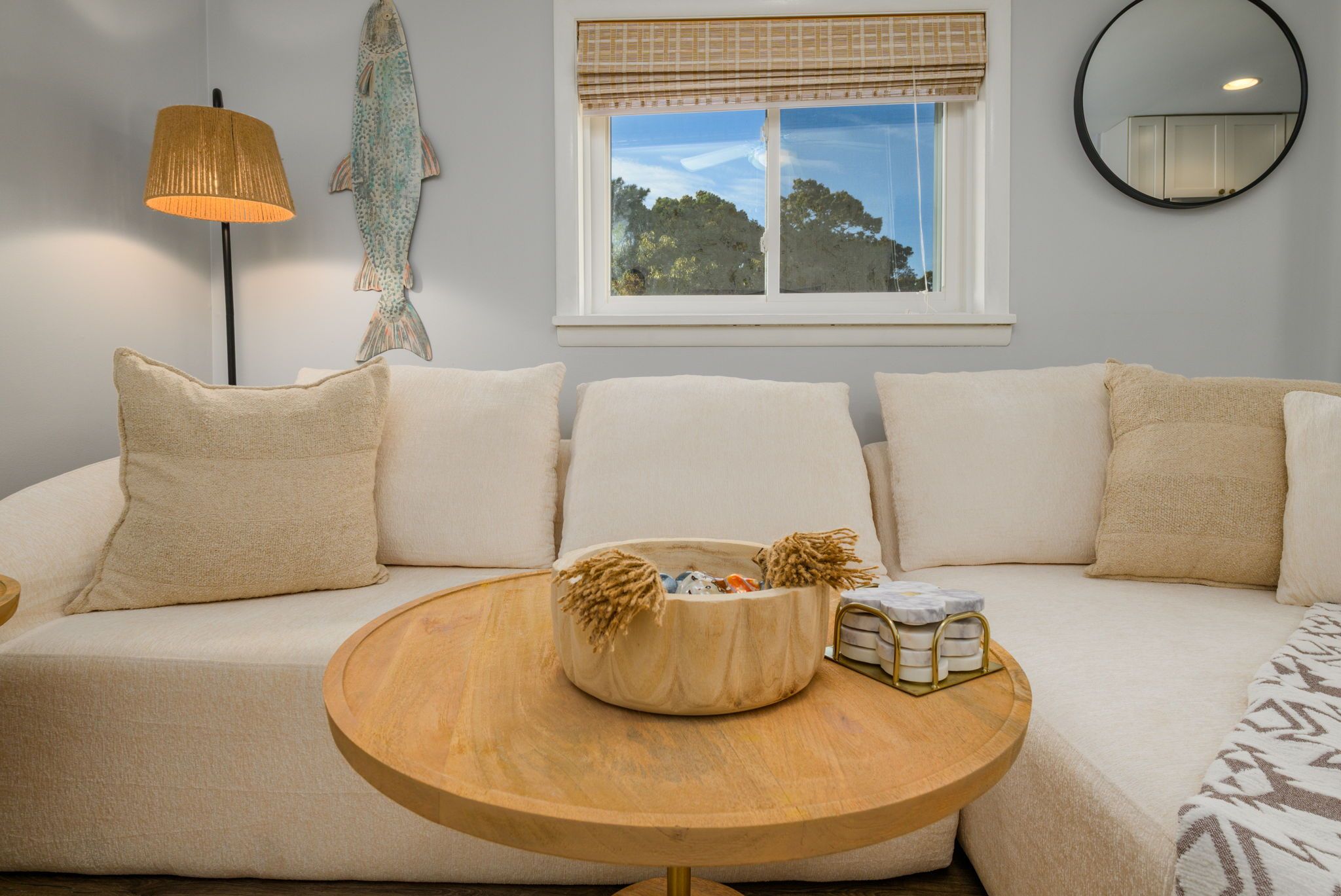Un salon moderne avec un canapé, une table basse ronde en bois et une fenêtre donnant sur des arbres.