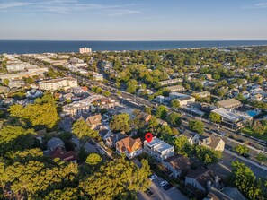 An aerial view of a residential area with a mix of single-family homes and commercial buildings, a main road, and a body of water in the distance.