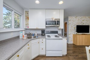 A modern kitchen with white cabinets, a built-in microwave, a stove, and a coffee maker.