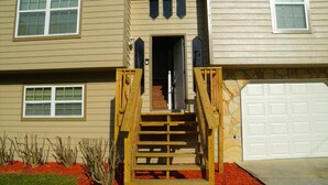 A two-story house with a wooden staircase leading to the front door, a garage door, and a stone accent wall. - Spacious Home Near Atlanta, Sweetwater Park, Six Flags and Airport (Lithia Springs)