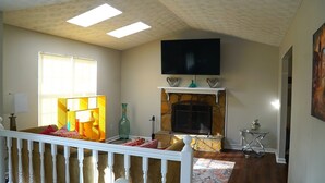 A living room with a fireplace, a television mounted above it, and a window with blinds. - Spacious Home Near Atlanta, Sweetwater Park, Six Flags and Airport (Lithia Springs)