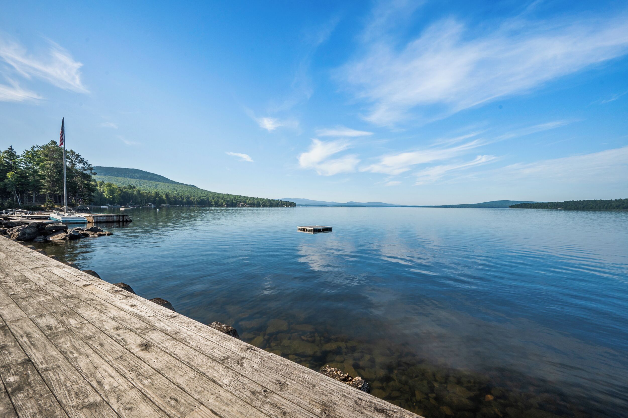 A calm lake with a wooden dock, boats, and a flagpole.