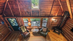 A cozy cabin interior with a fireplace, two leather chairs, a round coffee table, and a view through large windows. - Haines Landing - 7 Spruce Street - shared waterfront on Mooselook (Oquossoc)