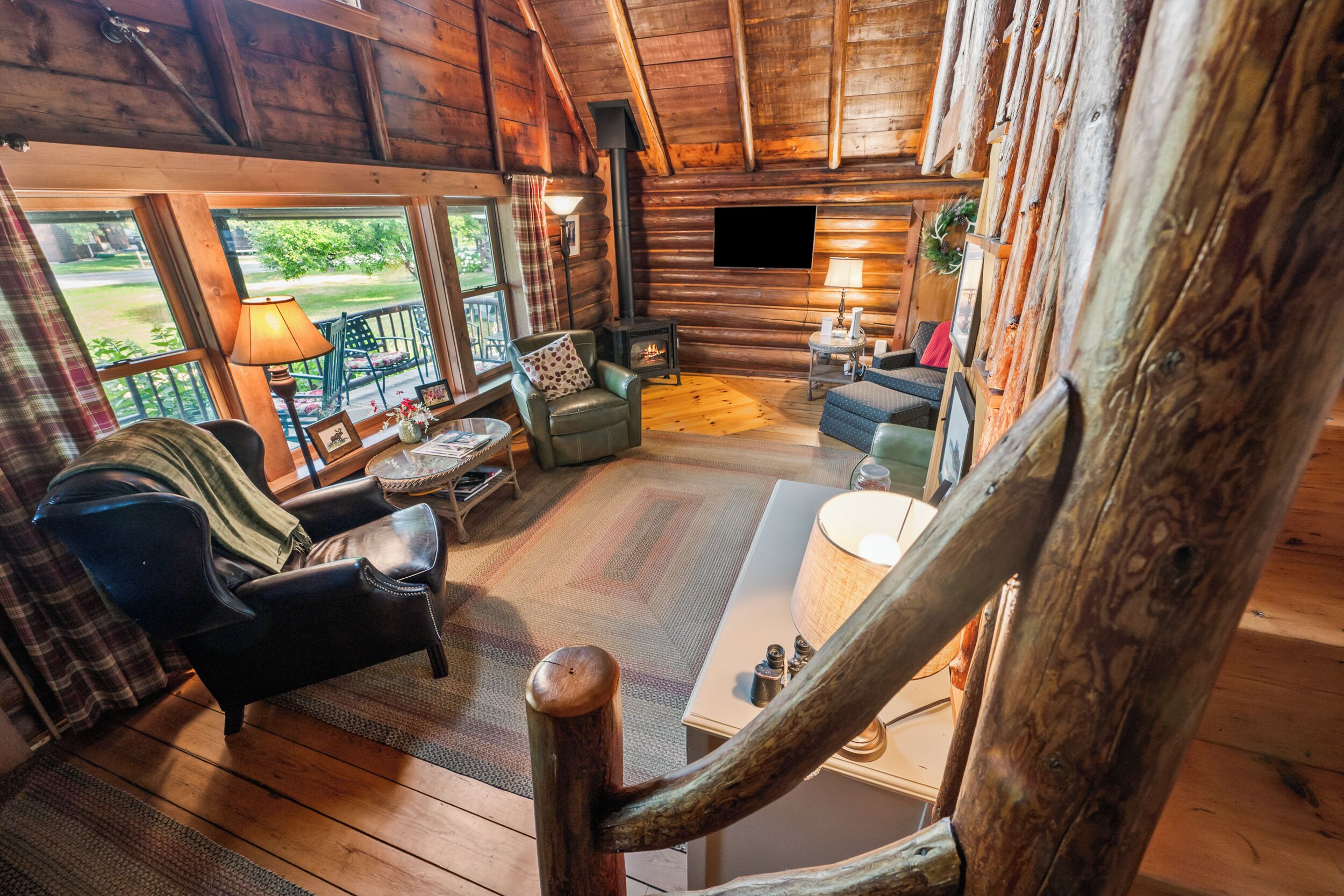 A log cabin interior with a fireplace, seating area, and large windows.