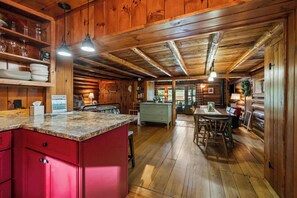 Interior de una cabaña con cocina, que incluye armarios de madera, una encimera roja y una mesa de comedor con sillas.