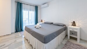 Ein Schlafzimmer mit einem Bett, zwei Nachttischlampen, einem Nachttisch, einem Fenster mit Vorhängen und einer Klimaanlage.