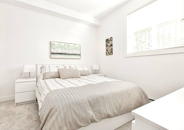 A minimalist bedroom with a bed, nightstands, a window, and wall art.