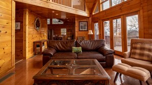 Un acogedor interior de cabaña con detalles de madera, un sofá de cuero, un sillón de cuadros y una mesa de centro de vidrio.