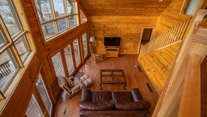 Un interior de cabaña de madera con un sofá de cuero, un televisor y una escalera.